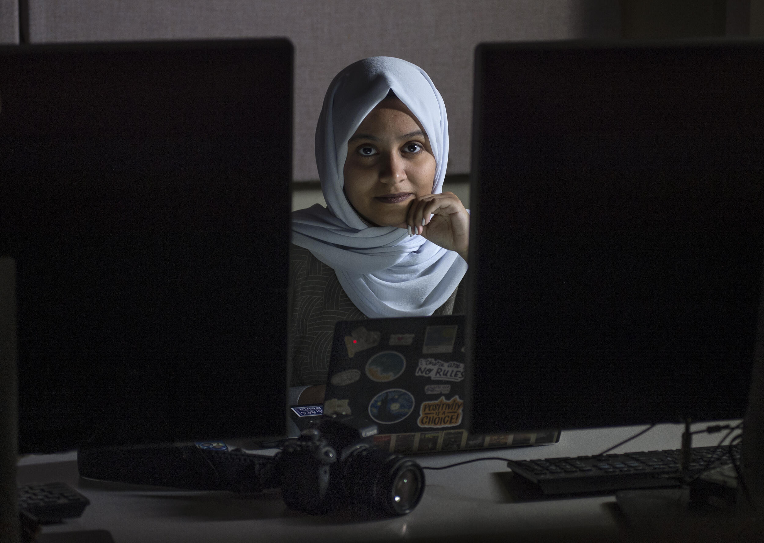 A photo of a woman sitting between two computer monitors with a laptop in front of her 