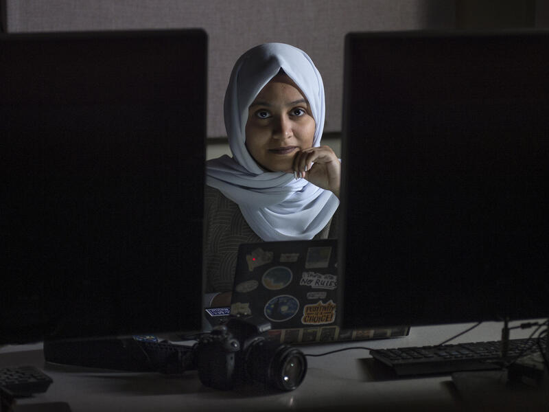 A photo of a woman sitting between two computer monitors with a laptop in front of her 