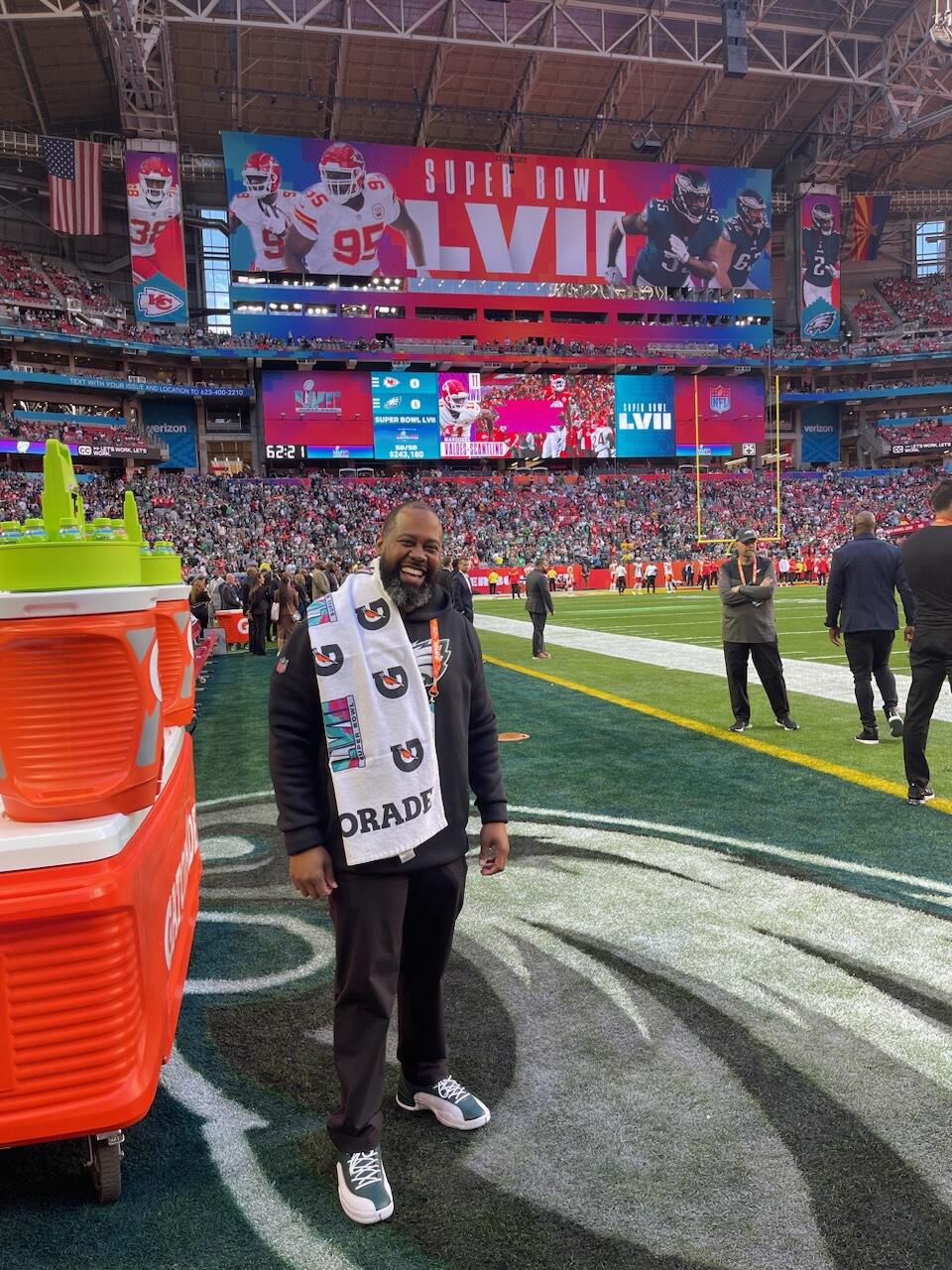 A man standing on a football field in a stadium while smiling. 