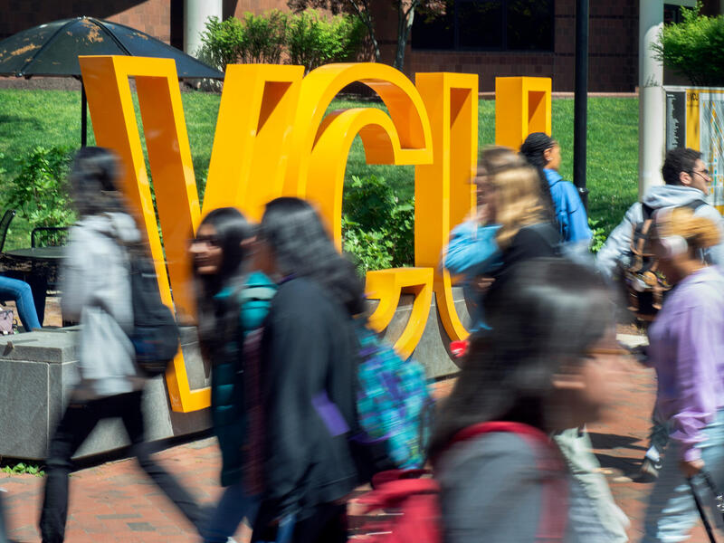 Students walk in front of a yellow VCU sign.