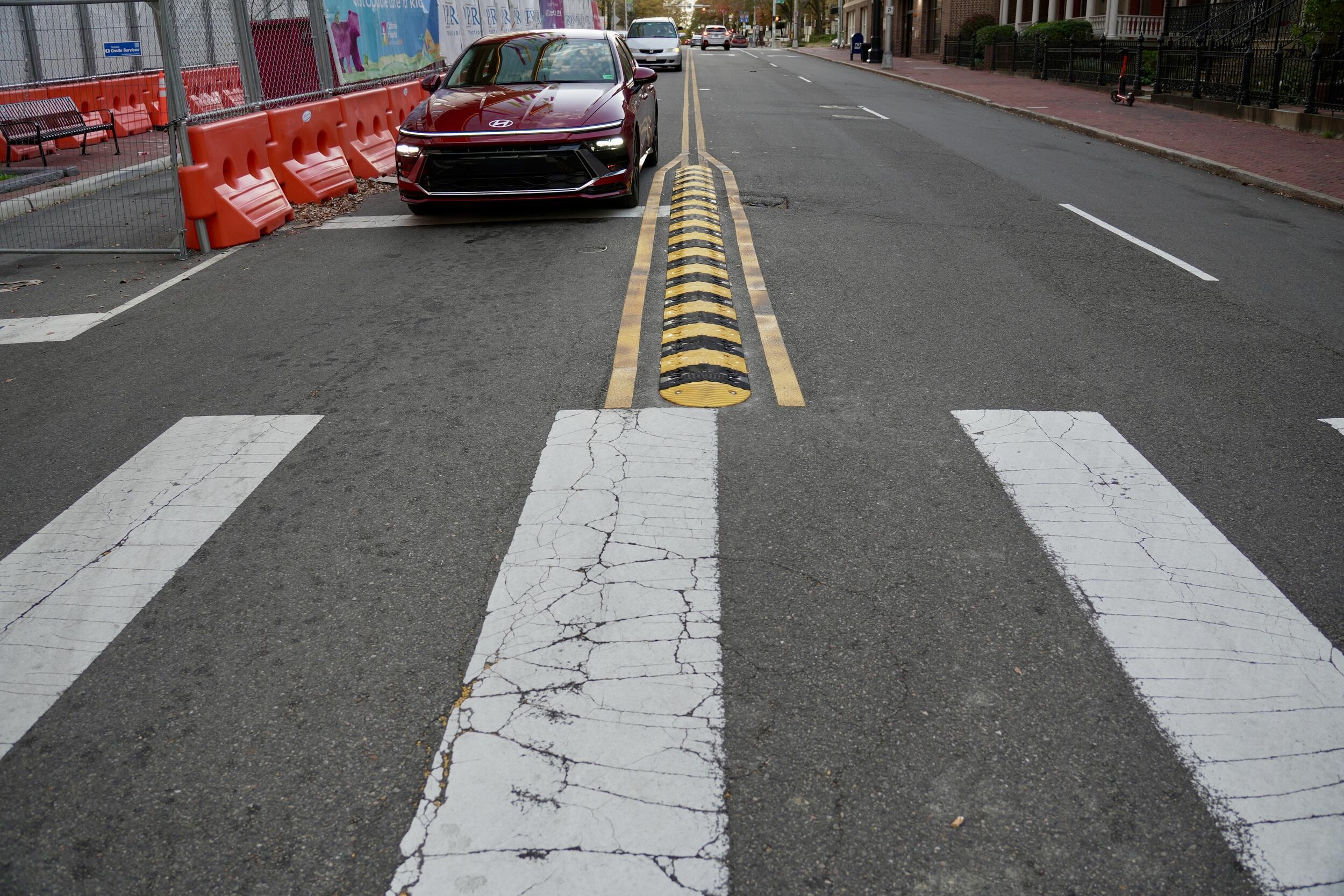 A photo of a car next to a cross walk and speed bump. 