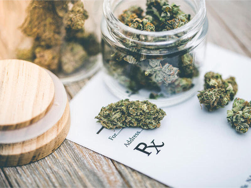 A photo of an open jar full of marijuana on top of a piece of paper for a prescription.