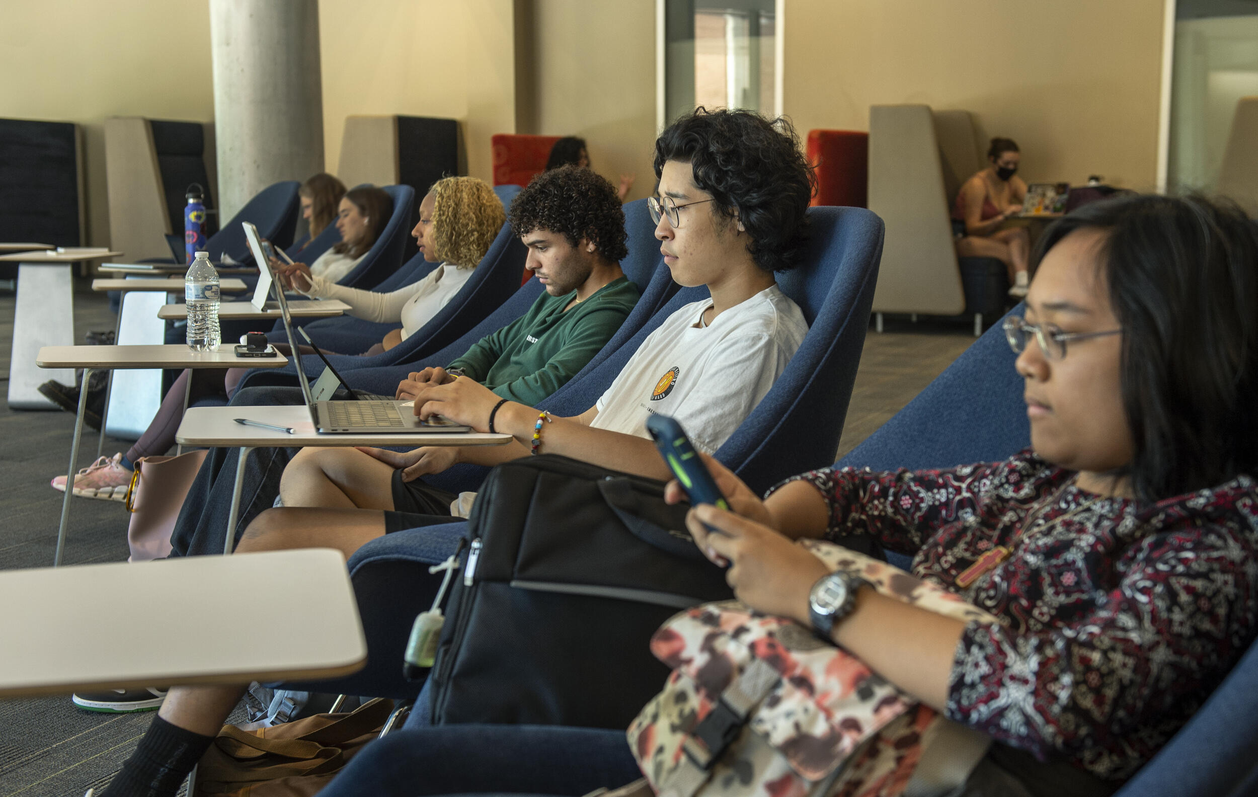 Six students sitting in chairs with small desks in front of them. 