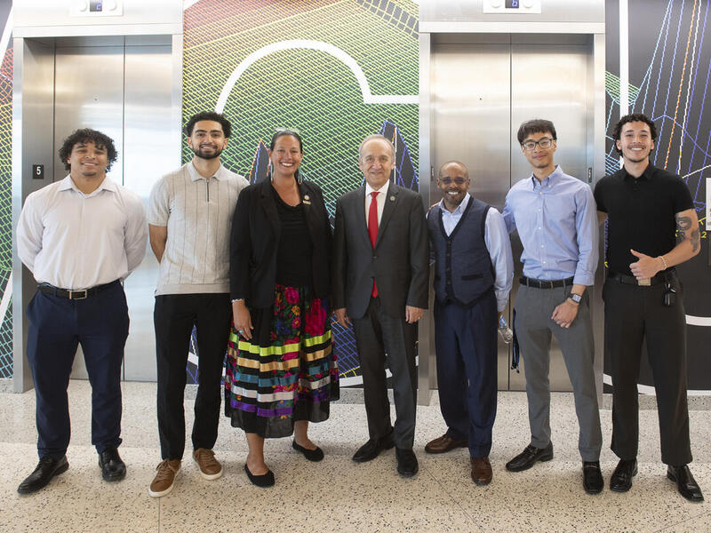 A group photo of seven people standing in front of a set of elevators. 