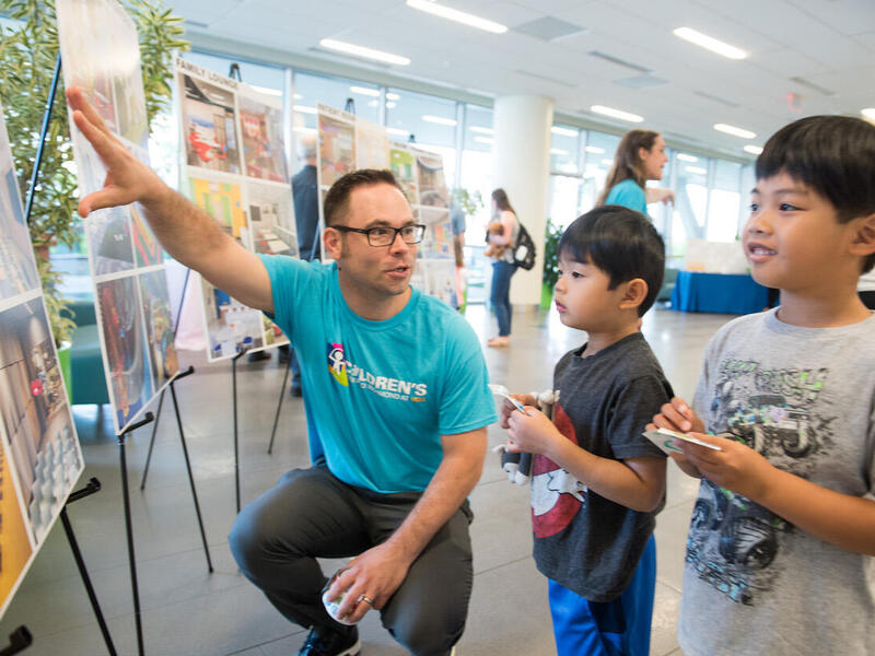 Adult man shows images of a new children's hospital to two children.