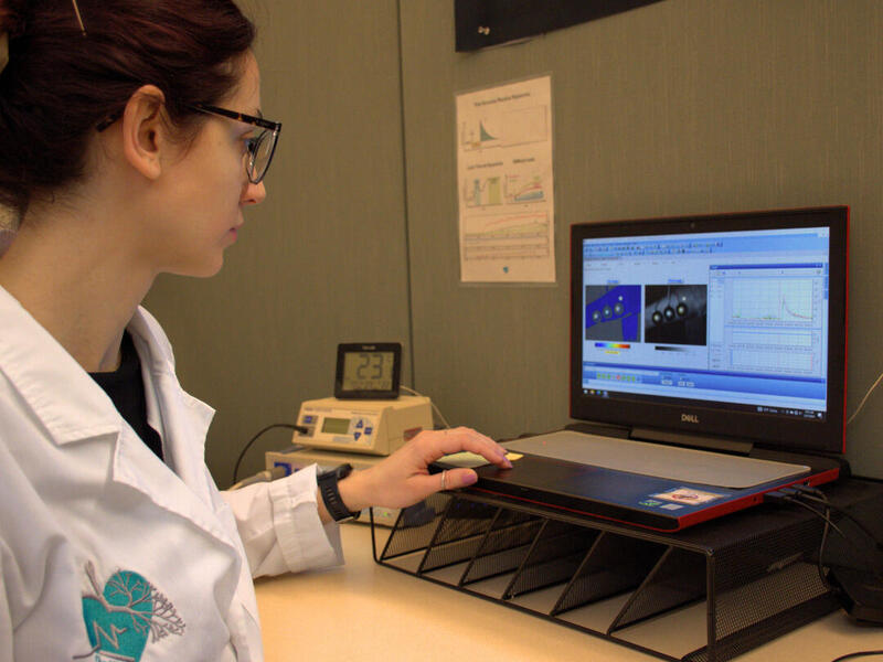 A photo of a woman in a lab coat looking at a lap top on a table 