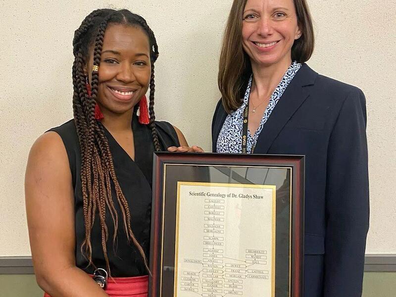 Two women standing next to each other, one is holding a framed document 