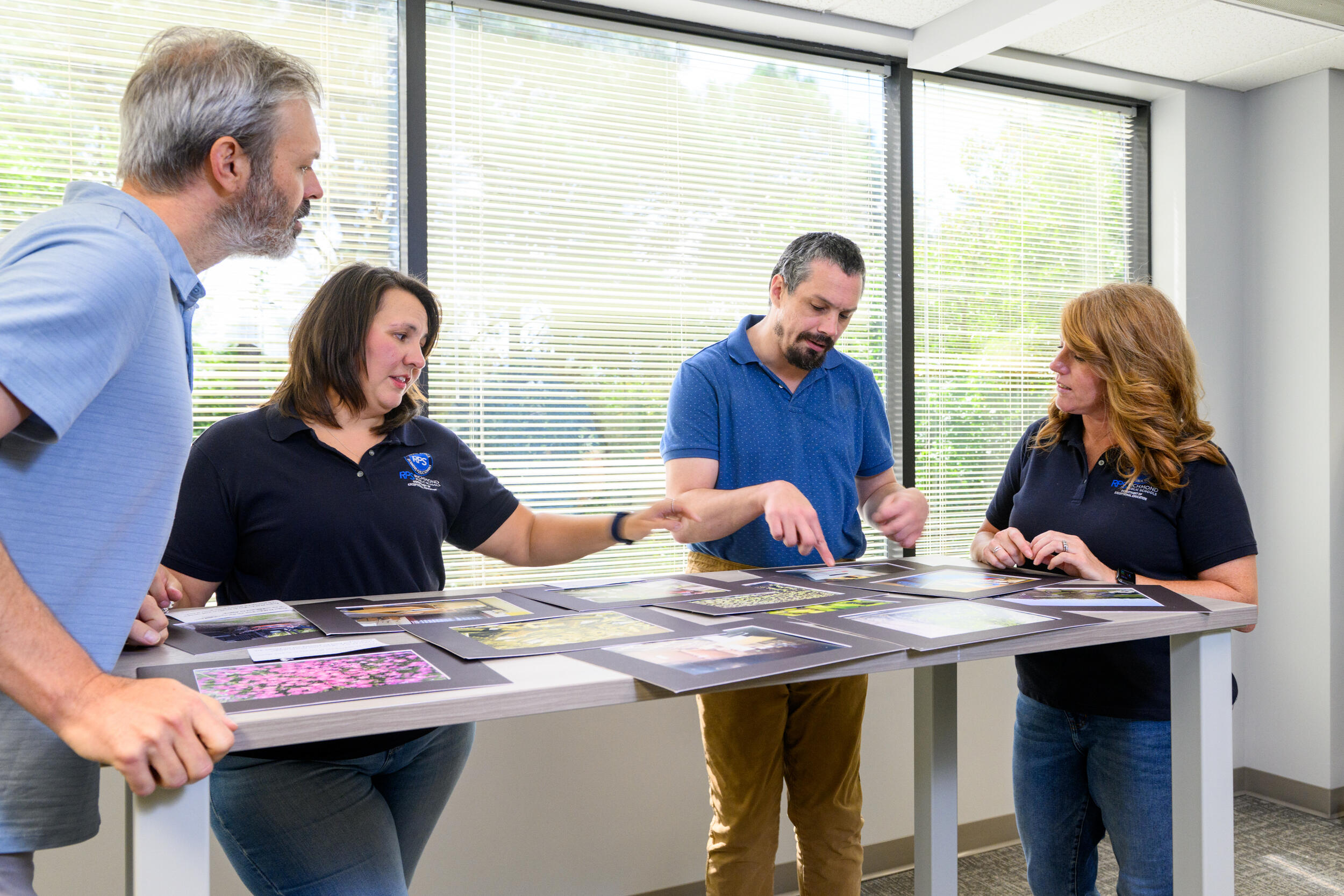 A photo of four people looking at photos that are on a table. 