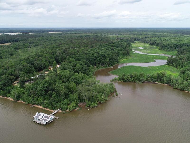 An aerial photo of the James River next to a forest and wetland. On the treeline is a doc leading to a building. 