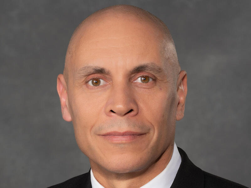A photo of a bald man wearing a suit and tie from the shoulders up. 