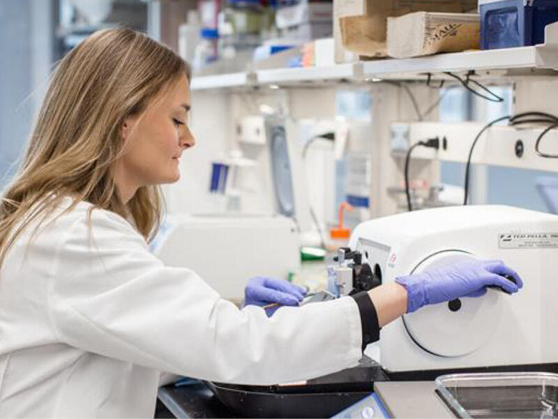 A woman wearing a labcoat and blue gloves 