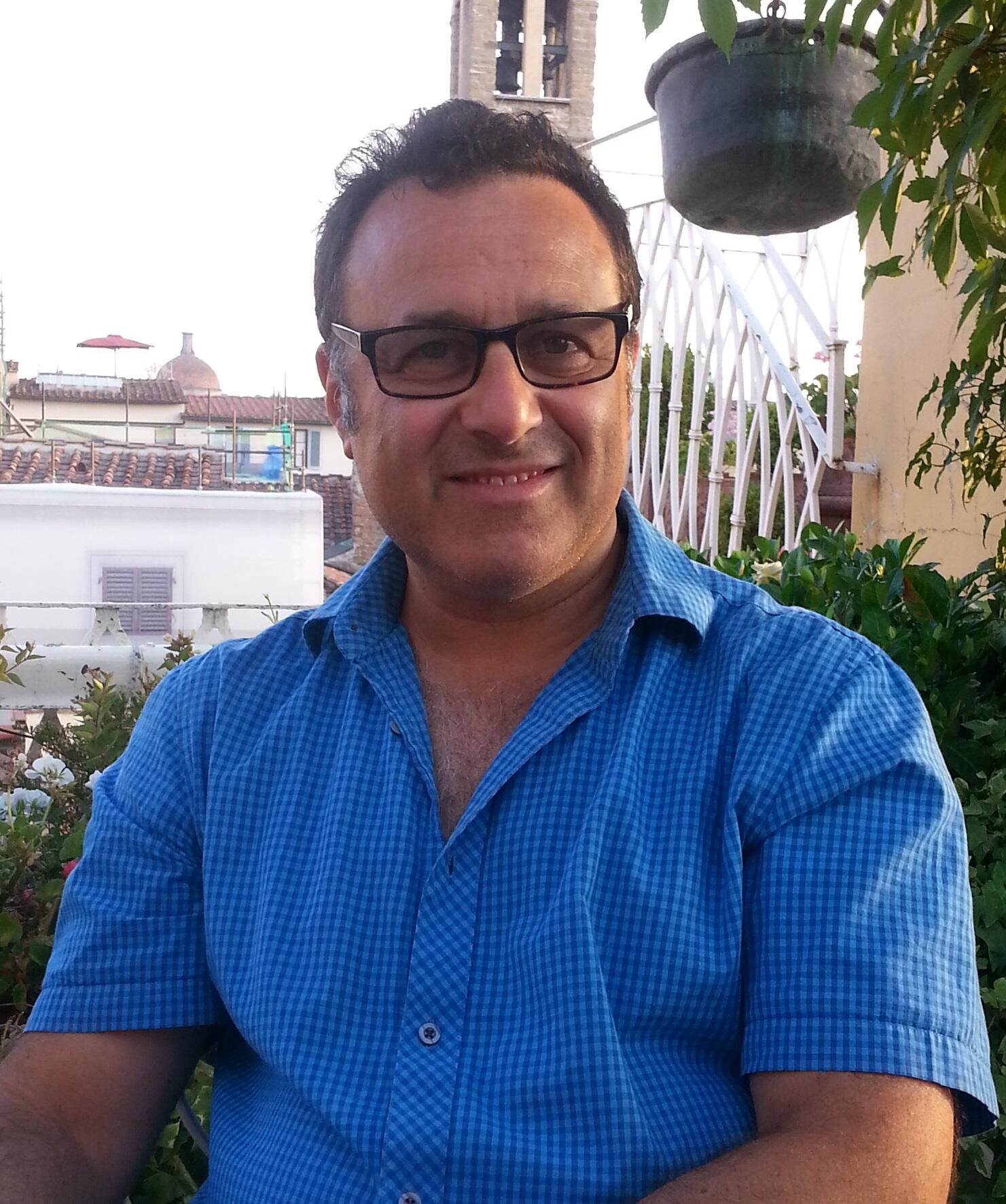 A portrait of a man wearing a blue short sleeve shirt with a collar and glasses. 