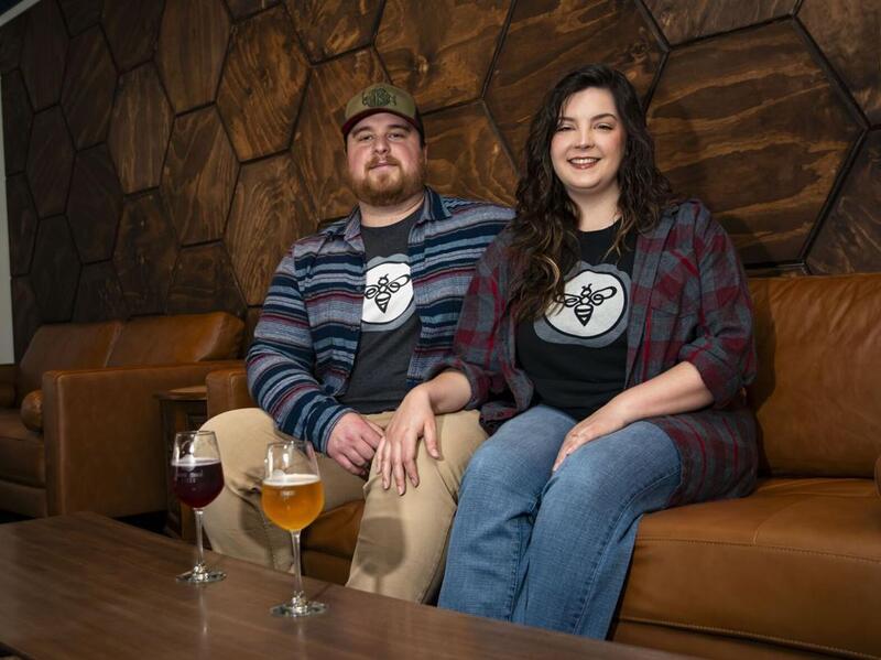 A photo of a man and a woman sitting on a brown leather couch. In front of the couple is a wooden coffee table with two tall stemmed glasses of cider on it. 
