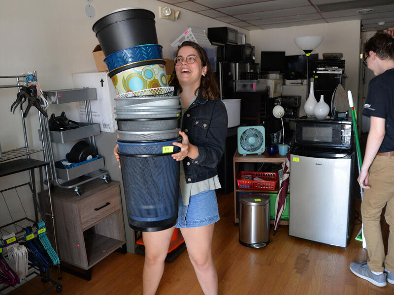 A smiling woman holding a stack of garbage bins.