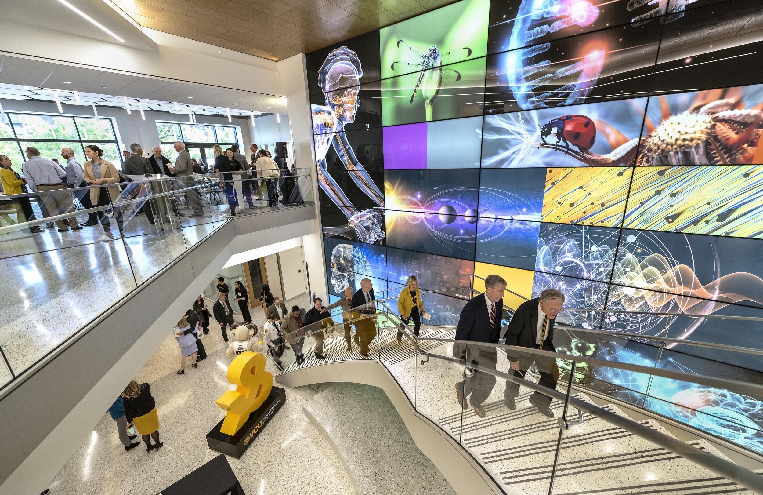 A photo of a lobby with a staircase and a wall full of lit up images.