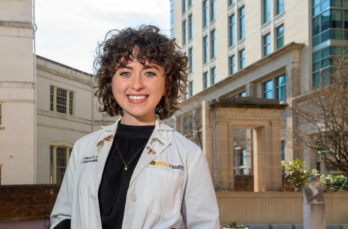 Laura Ellis smiling and wearing a white lab coat that says \"VCU Health\" 
