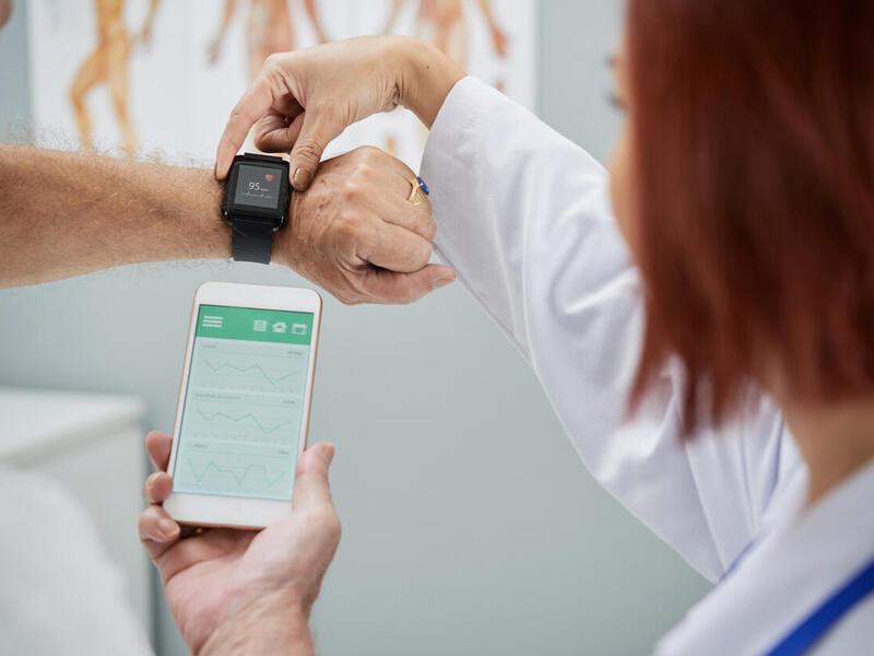 A doctor reviews information on a patient's smartwatch and phone.