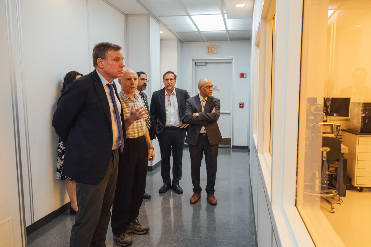 People in a hallway looking through a window into another room 