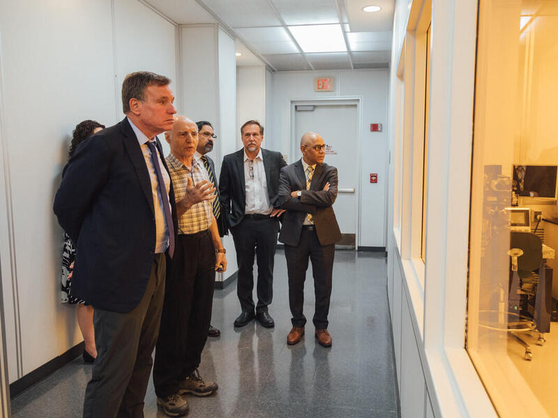 People in a hallway looking through a window into another room 