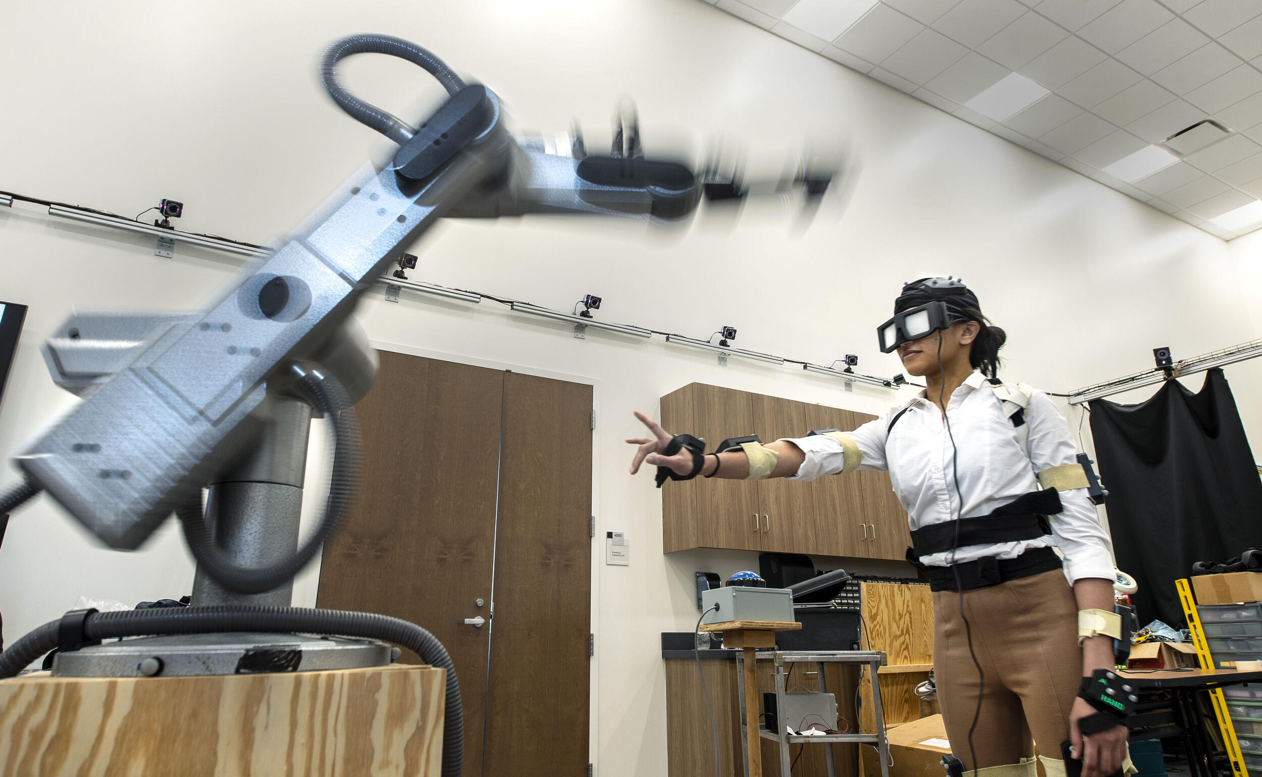 Person in motion-capture suit reaches out her hand toward a robotic arm.