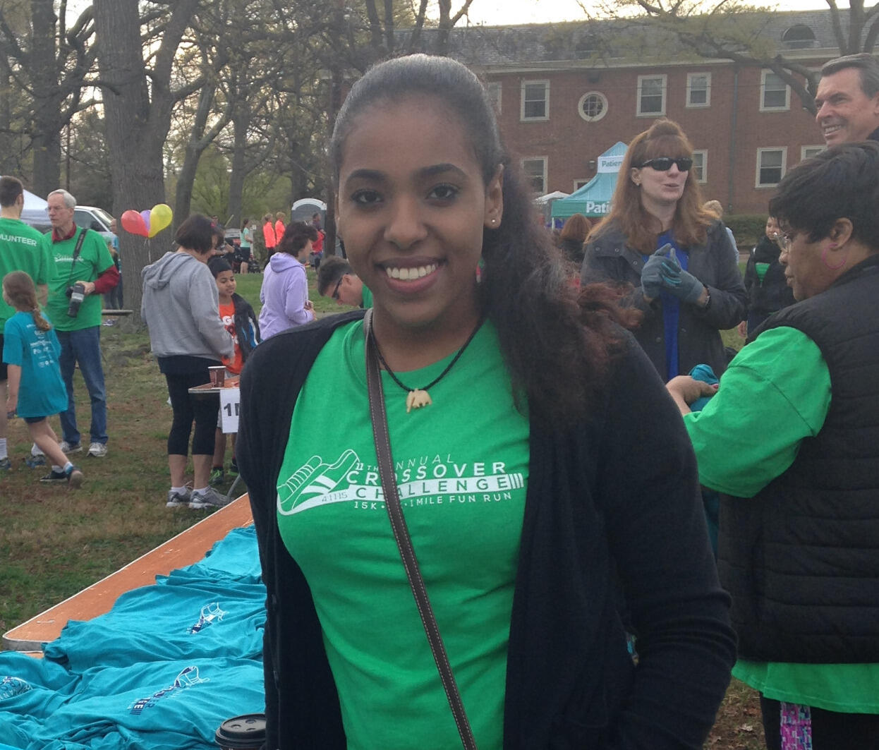 A woman in a green shirt smiles and leans on a table filled with T-shirts.