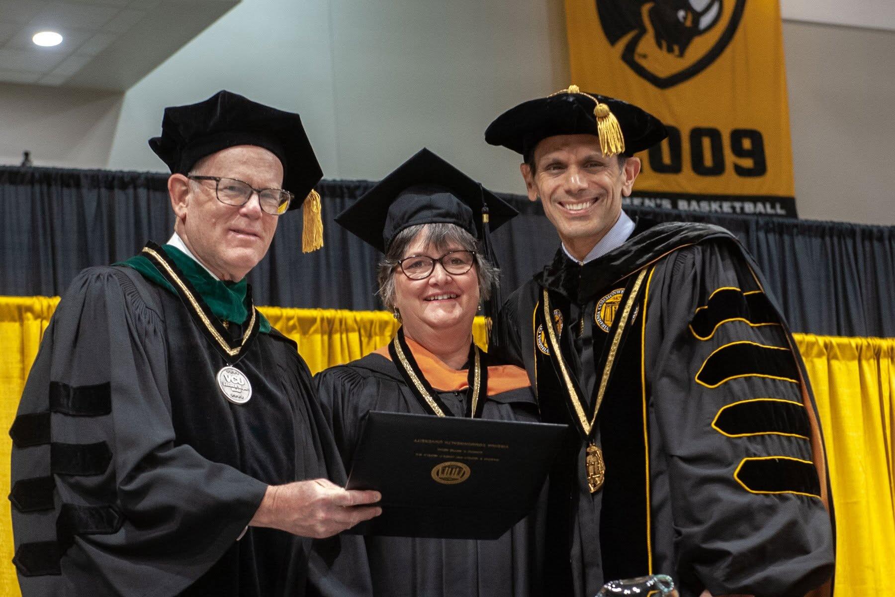 A photo of three people wearing graduation cap and gowns. 