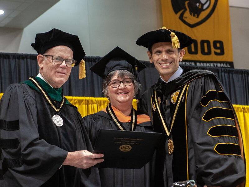 A photo of three people wearing graduation cap and gowns. 