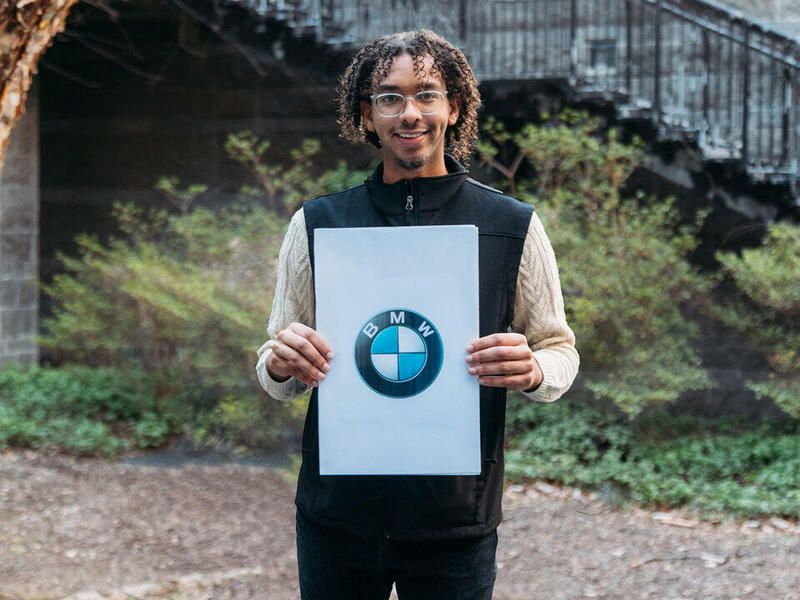A photo of a man standing outside holding a piece of paper with the BMW logo on it. 