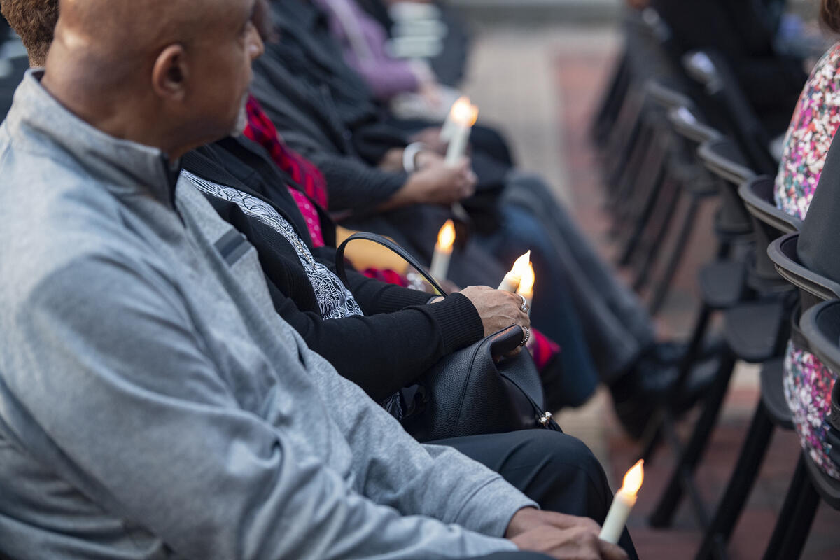 People sitting in rows of chairs holding candles. 