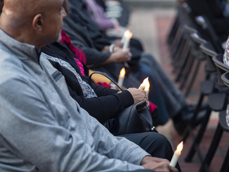 People sitting in rows of chairs holding candles. 