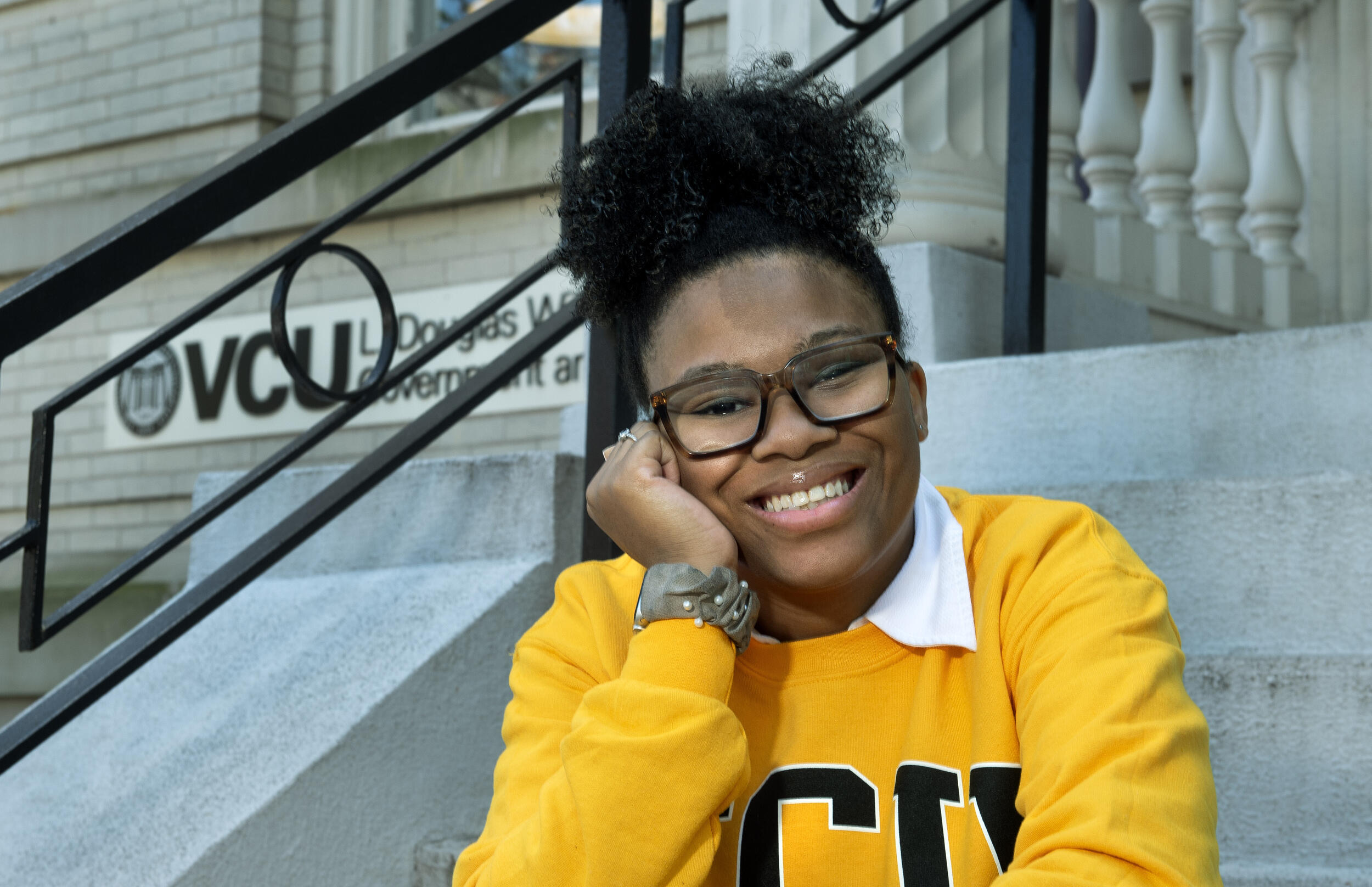 A photo of a woman smiling and resting her face on her right hand. 