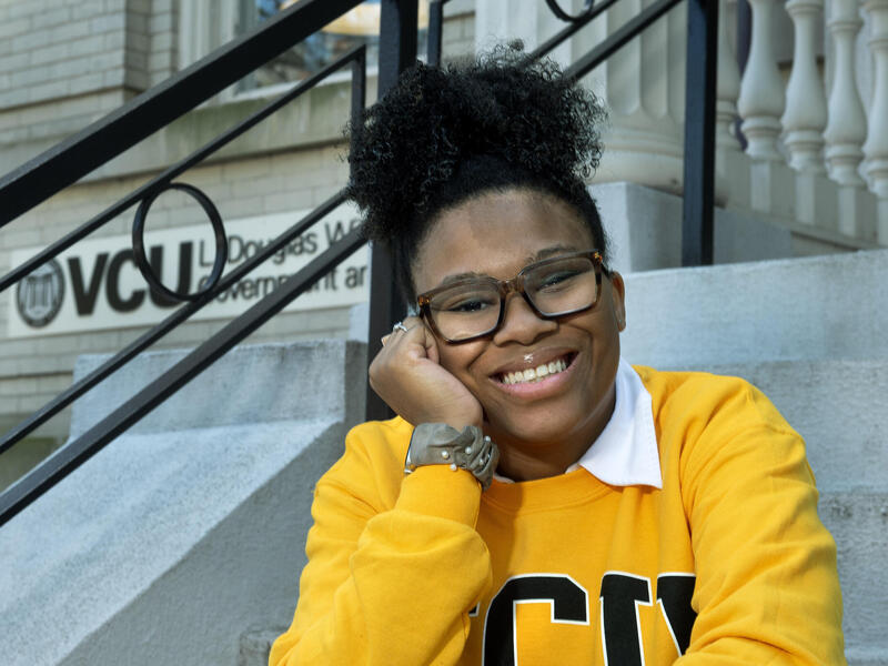 A photo of a woman smiling and resting her face on her right hand. 