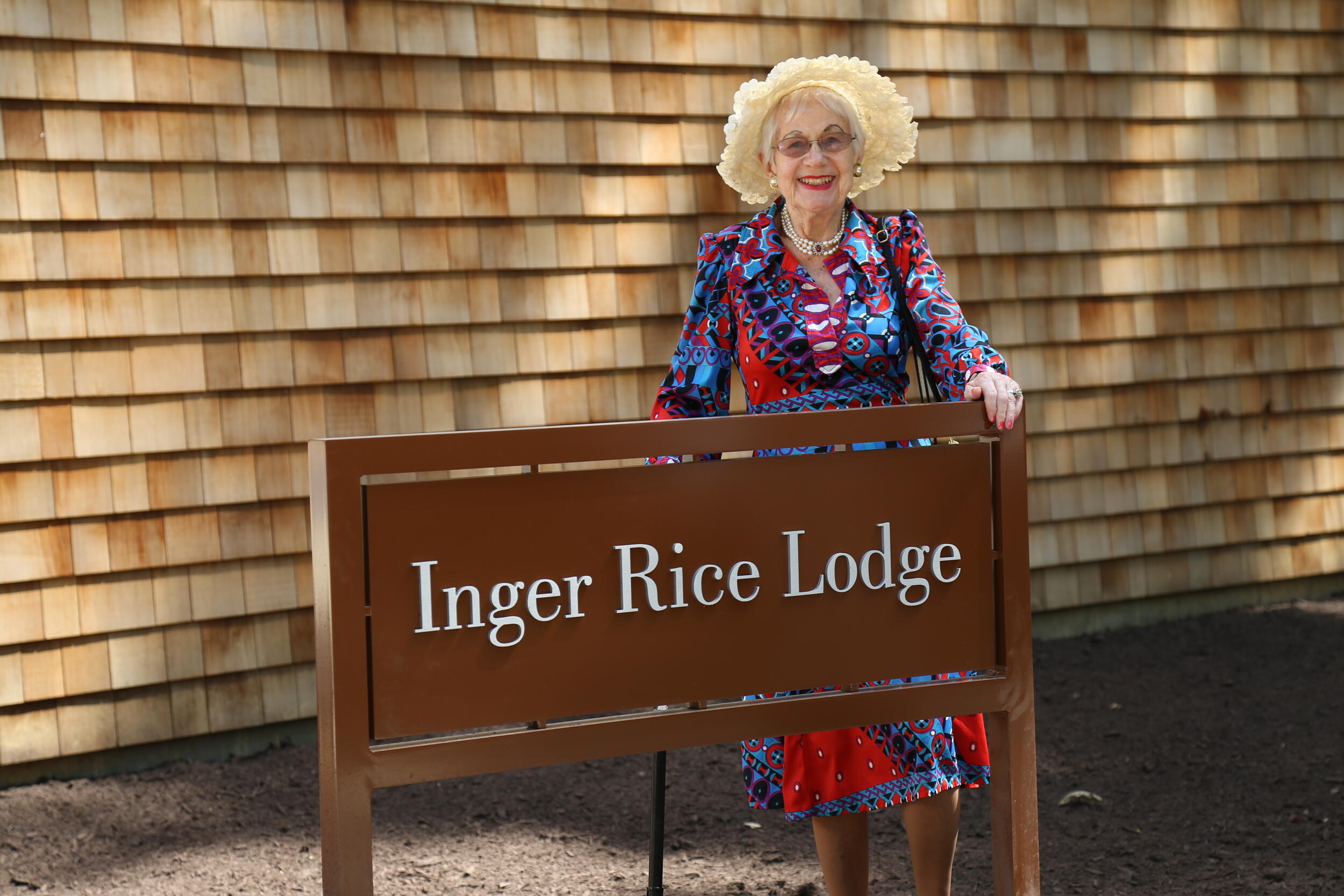 A photo of a woman smiling behind a brown sign that says \"Inger Rice Lodge\" in white letters. 