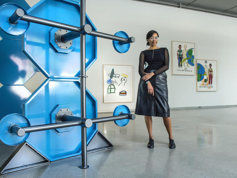 A person standing in an art gallery space. Various paintings hang on the walls behind them.