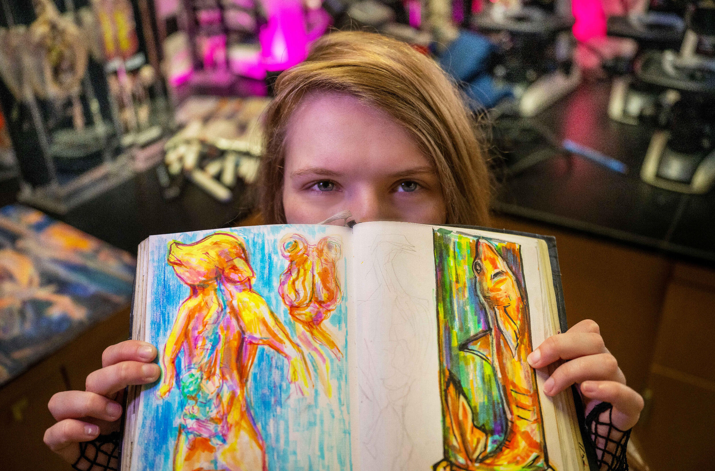 A woman holds bright illustrations of creatures in front of the bottom of her face.