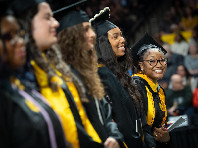 A row of five smiling women wearing caps and gowns.
