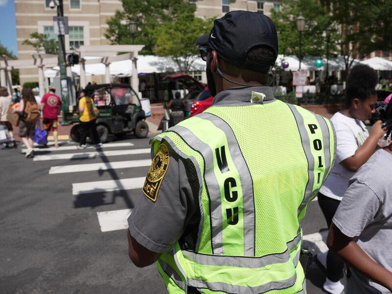 A photo of a police officer wearing a visability vest standing at a cross walk where people have just walked to the other side of the street. 
