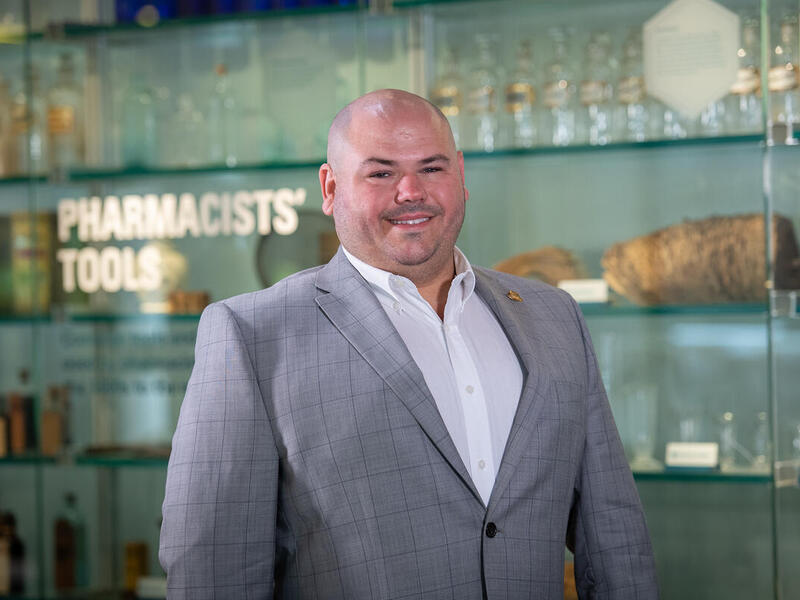 A photo of a man from the chest up. He is smiling and wearing a gray sports coat with a white button up shirt. 