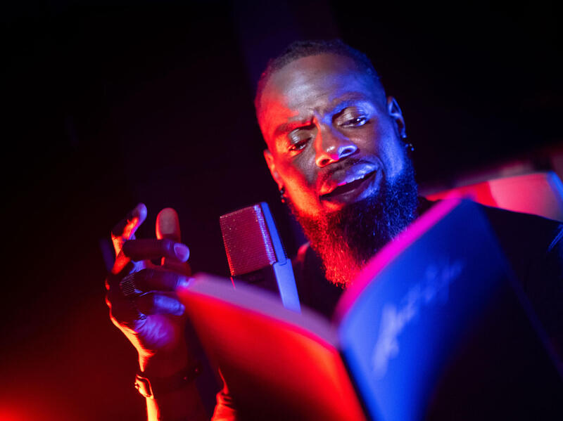 A man reads from a book, speaking into a microphone.
